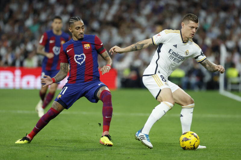El centrocampista alemán del Real Madrid Toni Kroos (d) disputa un balón ante el delantero brasileño del FC Barcelona Raphinha (i) durante el partido de la jornada 32 de LaLiga EA Sports entre Real Madrid y FC Barcelona (El Clásico), en el estadio Santiago Bernabéu de Madrid. EFE/ Juanjo Martín