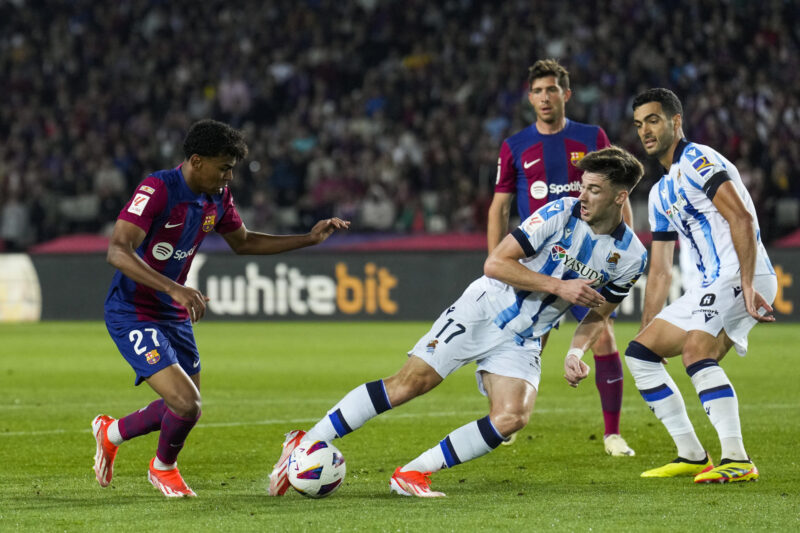 El delantero del FC Barcelona Lamine Yamal (i) lucha con el escocés Kieran Tierney, de la Real Sociedad, durante el encuentro correspondiente a la jornada 35 en Primera División que FC Barcelona y Real Sociedad disputan hoy lunes en el estadio Olímpico Lluis Companys, en Barcelona. EFE/Alejandro García