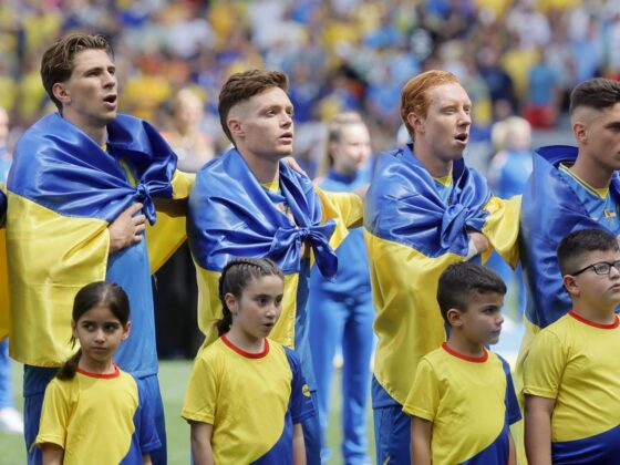Los jugadores de Ucrania, arropados de nuevo por su bandera Los jugadores de la selección ucraniana con la bandera de su país atada al cuello entonan el himno nacional en su debut en la Eurocopa 2024 contra Rumanía. EFE/EPA/RONALD WITTEK
