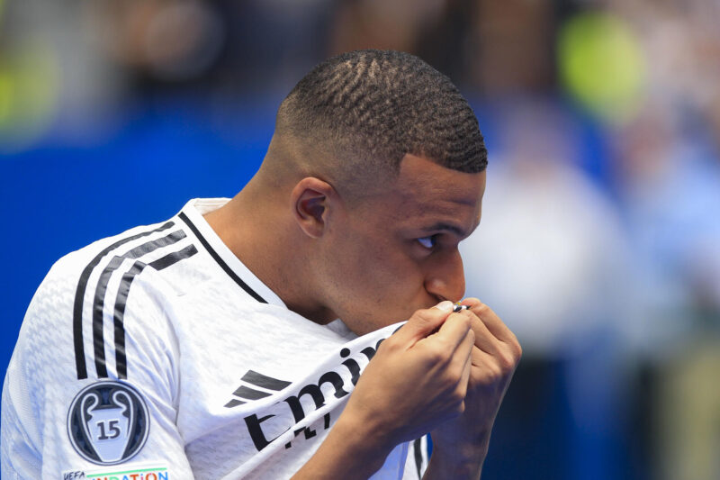 El francés Kylian Mbappé besa el escudo del Real Madrid durante su presentación como nuevo jugador del club, este martes en el estadio Santiago Bernabéu de Madrid. Mbappé ha firmado este martes el contrato que le une al conjunto blanco para las próximas cinco temporadas. EFE/Chema Moya