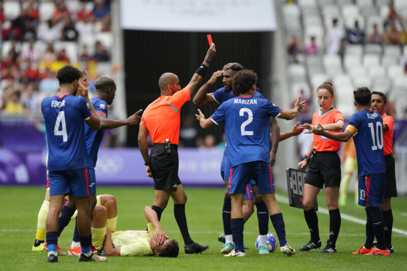 El árbitro Adel Al Naqbi (c) le saca la tarjeta roja al dominicano Edison Azcona (d) tras una acción contra Pau Cubarsí (en el suelo) durante el partido del Grupo C de fútbol masculino de los Juegos Olímpicos de París 2024 disputado este sábado en el Estadio de Burdeos. (Dominicana) EFE/ M. Reino